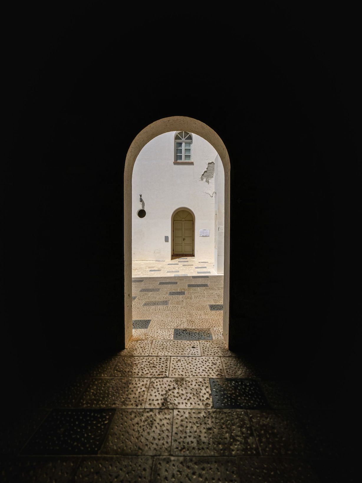 Un arco di pietra spessa che si apre su una corte bianca in pieno sole